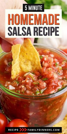 a person dipping salsa into a bowl with tortilla chips and tomatoes on the side