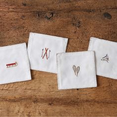 three white napkins with embroidered designs on them sitting on a wooden table next to each other