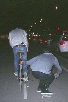 black and white photograph of two men on skateboards in the street at night time