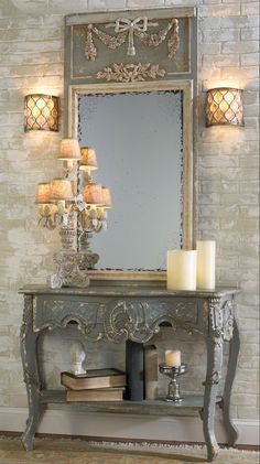 an ornate console with candles and a mirror on the wall next to it, in front of a brick wall