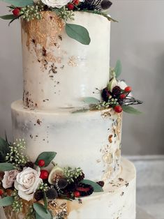 a three tiered white wedding cake with red berries and greenery