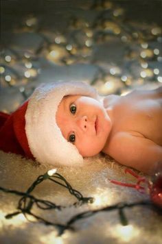 a baby wearing a santa hat laying on top of a bed next to christmas lights