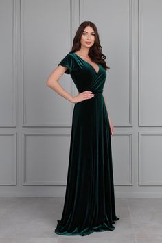 a woman wearing a green velvet gown with short sleeves and an open back, standing in front of a wall