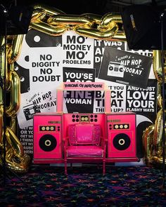 a pink chair sitting in front of a wall covered with posters and gold foil balloons