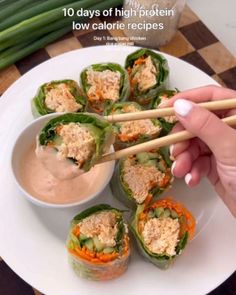 a person holding chopsticks up to some food on a plate with dipping sauce