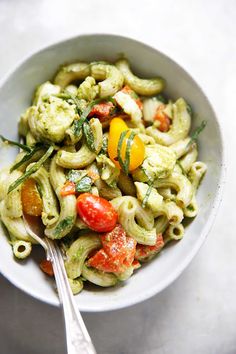 a white bowl filled with pasta and vegetables on top of a table next to a fork