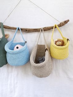 three crocheted baskets hanging from a wooden branch with two stuffed animals in them