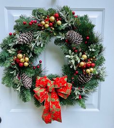 a christmas wreath on the front door with pine cones, berries and evergreens hanging from it