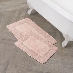 two bath mats sitting on top of a wooden floor next to a white tub in a bathroom