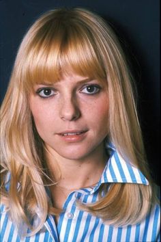 a woman with long blonde hair wearing a blue and white striped shirt looking at the camera