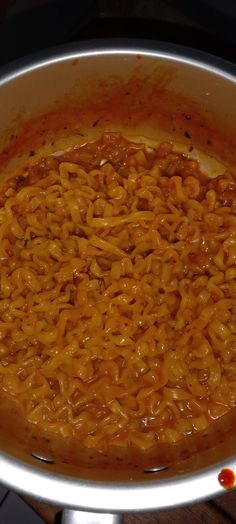 a large pot filled with noodles and sauce on top of a stove burner next to a wooden table