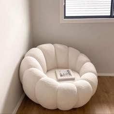 a white chair sitting in front of a window next to a book on a wooden floor