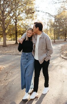 a man and woman are walking down the road in an open area with trees behind them