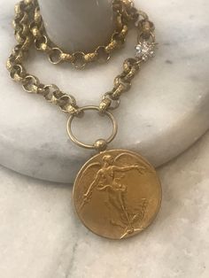 This beautiful statement necklace features an Angel medallion pendant with detailing on both and is 1.5 inches in diameter. It is antique gold plated. It hangs on a textured 8mm rolo chain in clear electroplated brass. Flower CZ connector adds a nice detail to the chain. It is offered in three length sizes: 16, 17 and 18. Choose from the menu. Lobster clasp. 🎁All orders are shipped in a box or a cloth pouch. Gift messages are attached to the box. Cheap Bronze Medallion Necklaces, Victorian Brass Jewelry With Coin Pendant, Victorian Brass Coin Pendant Jewelry, Gold Round Medallion Necklace With Charms, Yellow Gold Medallion Necklace With Large Brass Pendant, Yellow Gold Large Pendant Medallion Necklace In Brass, Gold Coin Necklace With Charms In Brass, Antique Gold Medallion Jewelry With Coin Pendant, Gold Medallion Necklace With Charms