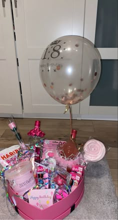 a pink basket filled with lots of items on top of a floor next to a balloon