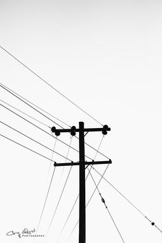 black and white photograph of an electric pole with power lines in the backgroud