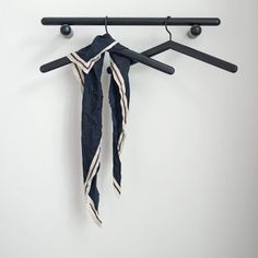 an umbrella hanging on a coat rack with two black hangers and one white striped scarf