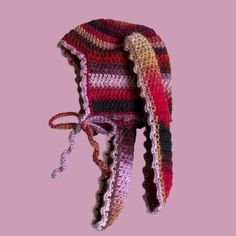 a multicolored crocheted hat hanging from a hook on a pink background