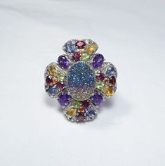 "The exquisite romance of a gem-encrusted four leaf clover is the setting for a brilliant rainbow druzy quartz that shimmers with blues, greens, golds and pinks. This exciting ring showcases the finest natural gemstones:  African amethyst, golden citrine, Rhodolite garnet, peridot, tanzanite, fire opal and red garnet. This gothic beauty is further enhanced by an ornate milgrain detail of sterling silver that traces the stones throughout the gallery and around the center druzy. On the shoulders, Clover Ring, Druzy Quartz, Gothic Beauty, Rhodolite Garnet, Four Leaf, Leaf Clover, Four Leaf Clover, Red Garnet, Fire Opal