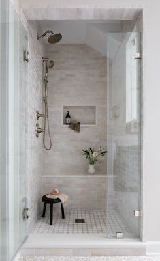 a walk in shower sitting next to a white tiled wall and floor with a bench on the side