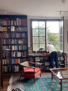 a man standing in front of a bookshelf filled with lots of books next to a window