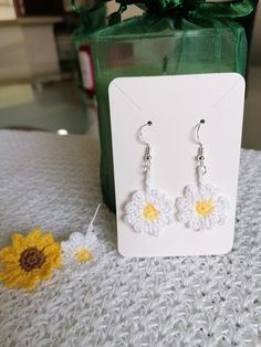 a pair of white crochet flower earrings sitting on top of a table next to a green bag