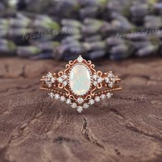 a white opal and diamond ring sitting on top of a piece of wood