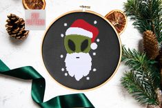 a cross stitch christmas ornament with an alien wearing a santa hat