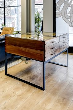 a desk with drawers and a plant on top in front of large windowed windows