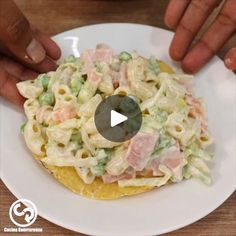 two hands reaching for a pasta dish on a white plate with green peas and ham