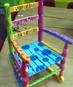 a colorful wooden rocking chair sitting on top of a table next to a sign that says laugh out loud believe in magic follow your heart