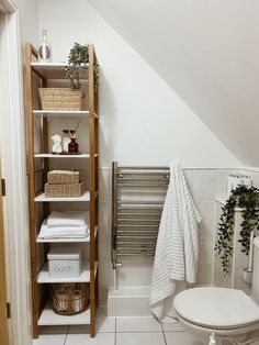 a bathroom with white walls and tile flooring next to an open toilet, shelving unit and towel rack