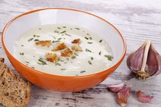 an orange bowl filled with soup next to garlic and bread