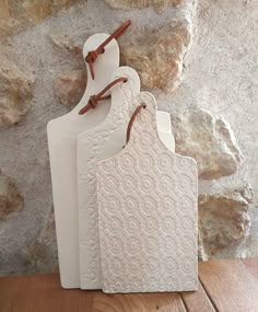 three white ceramic cutting boards sitting next to each other on a wooden table in front of a stone wall