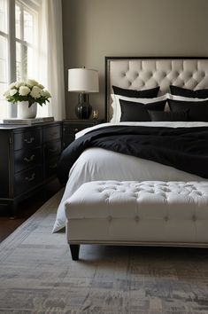 a white bed with black and white pillows in a bedroom next to a large window