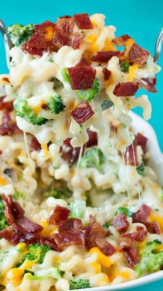 broccoli and bacon macaroni salad is being lifted from a white bowl