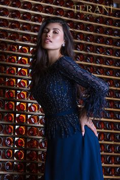 a woman in a blue dress standing next to a wall full of wine bottle bottles