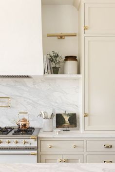 a kitchen with white cabinets and marble counter tops, gold trim on the oven hood