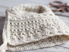 a white crocheted hat sitting on top of a wooden table next to scissors