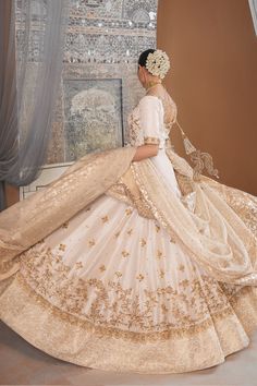 a woman in a white dress is standing near a window and wearing a tiara