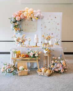 a table topped with lots of food and flowers next to a wall covered in balloons