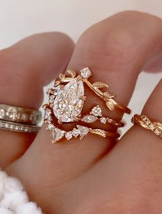 a woman's hand with three different rings on top of each other and one has a pear shaped diamond in the middle