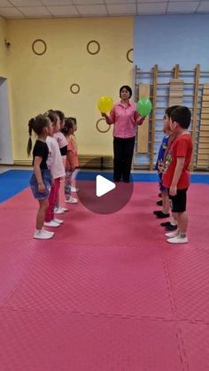 a group of children standing in a room with one person holding balloons and the other looking at them