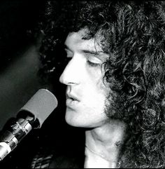 a black and white photo of a man with curly hair in front of a microphone