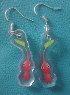 two red fish shaped glass earrings on a blue surface