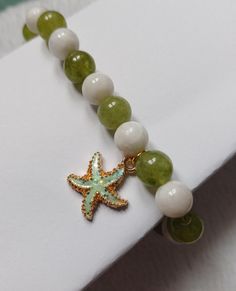 Fit wrist 8" down Lovely round beads in green and white Gorgeous enamel coated starfish charm, all on a strong elastic Handmade White Starfish Bracelets, White Starfish Charm Bracelet, White Starfish Bracelet With Ocean-inspired Style, White Ocean-inspired Starfish Bracelets, White Starfish Ocean-inspired Bracelet, Ocean-inspired White Starfish Bracelet, Adjustable White Jewelry With Starfish Charm, White Beaded Bracelet With Starfish Charm As Gift, White Adjustable Beaded Bracelet With Starfish Charm