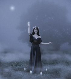 a woman in a black dress holding an object up to the sky with candles around her