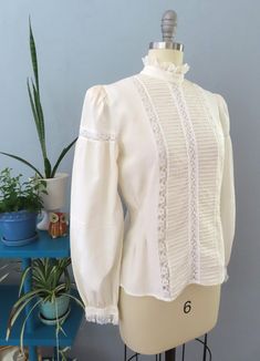 Vintage 80's Victorian blouse. Off white silk with high lace ruffle collar, eyelet lace, horizontal pleats and button lace cuffs. Button down back with billowy long sleeves with puffed shoulders. Sightly sheer overall. Straight hem. Gorgeous top would be great for a formal event.  Fits up to a size large. Please double-check the measurements below: MEASUREMENTS--Taken with garment laying flat, in inches, doubled: Bust: 40"  Waist: 38"  Shoulder: 14" Length: 23" {top neck to bottom hem} Neck: 14" Victorian Fitted Ruffle Blouse, Victorian Fitted Ruffled Blouse, Fitted Victorian Blouse With Ruffles, Feminine Formal Tops With Lace Cuffs, Formal Fitted Blouse With Ruffled Collar, Fitted Lace Blouse With Ruffles, Chic Ruffled Lace Top For Wedding, Fitted Blouse With Lace Trim For Workwear, Chic Lace Top With Ruffles For Wedding