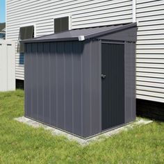 a gray shed sitting in the grass next to a house