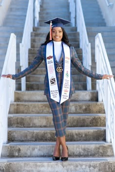 a woman wearing a graduation cap and gown standing on some stairs with her arms outstretched